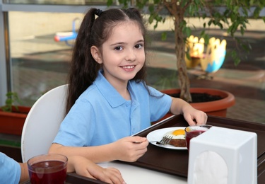 Photo of Cute girl at table with healthy food in school canteen