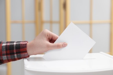 Photo of Woman putting her vote into ballot box on blurred background, closeup