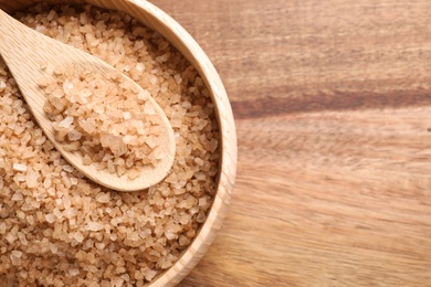 Photo of Bowl and spoon with brown sea salt on wooden table, top view. Spa treatment