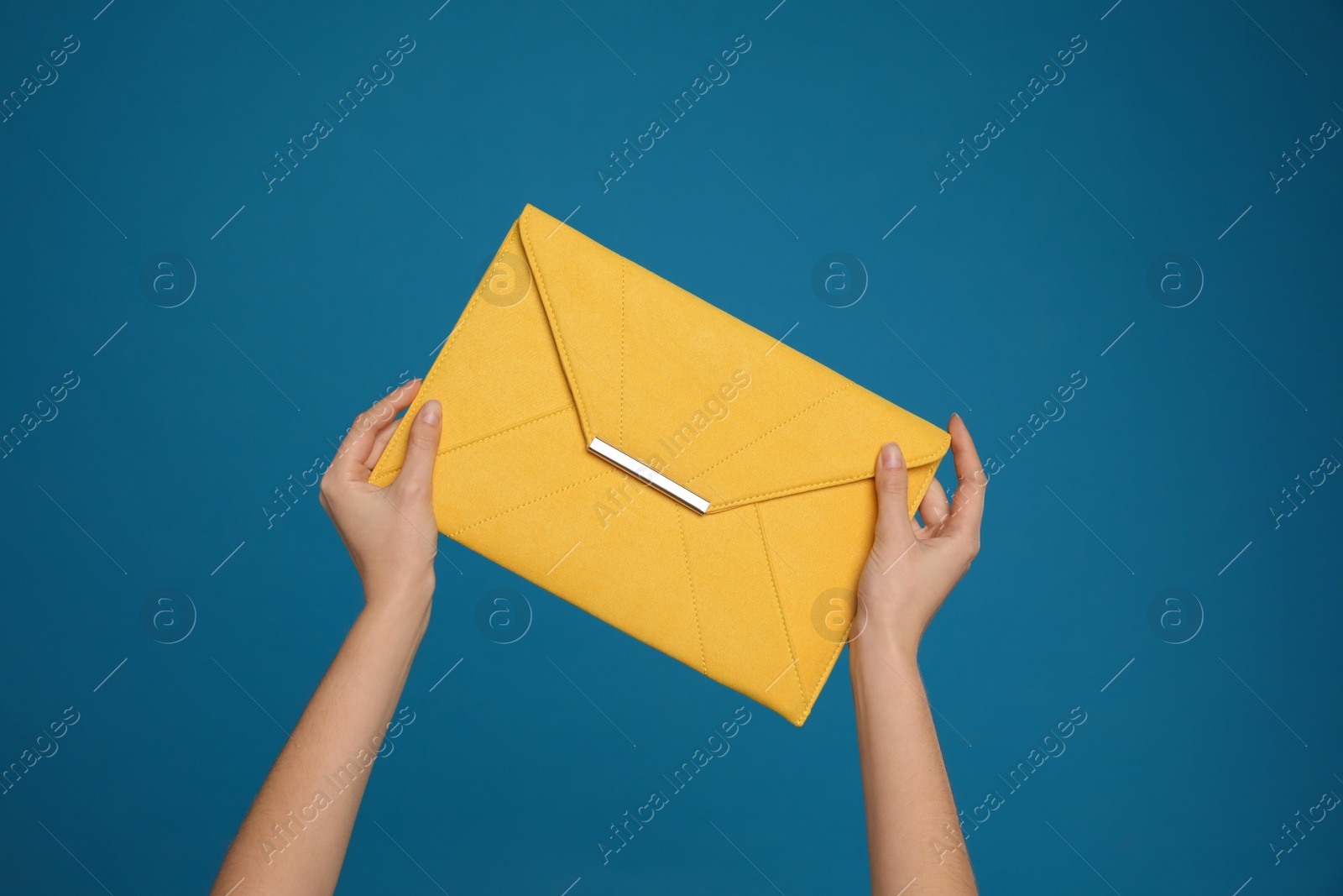 Photo of Woman holding stylish envelope bag on blue background, closeup