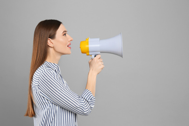 Young woman with megaphone on light grey background