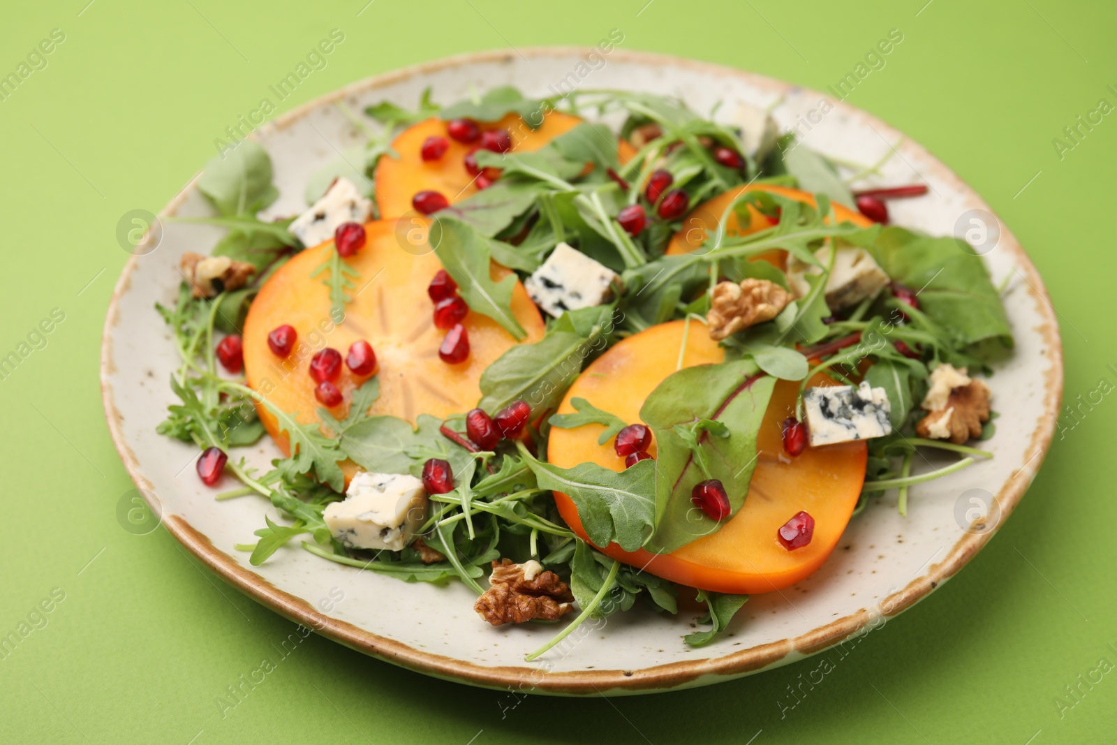 Photo of Tasty salad with persimmon, blue cheese and walnuts served on light green background
