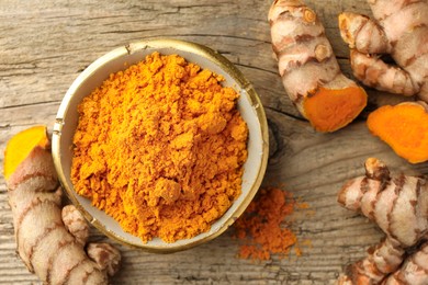 Photo of Aromatic turmeric powder and raw roots on wooden table, flat lay