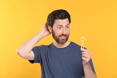 Photo of Confused man with tongue cleaner on yellow background