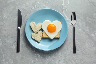Romantic breakfast with heart shaped fried egg and toasts served on grey marble table, flat lay