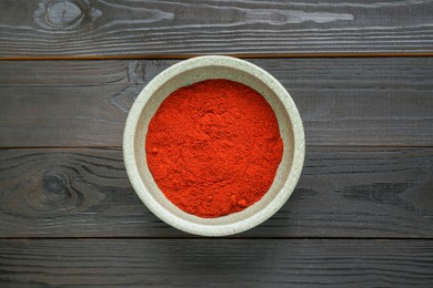 Bowl of aromatic paprika on black wooden table, top view