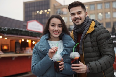 Photo of Young couple with cups of mulled wine at winter fair. Space for text