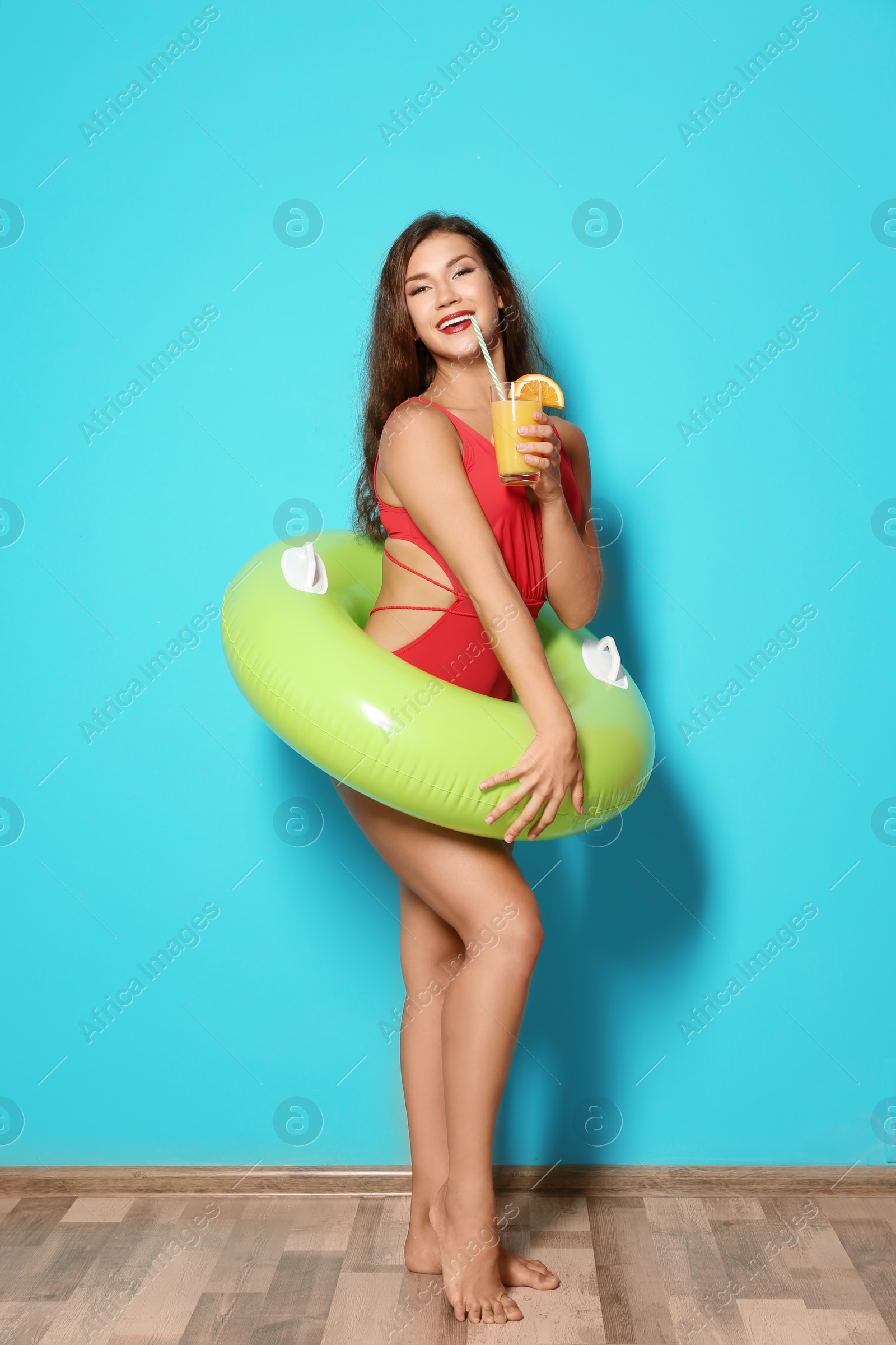 Photo of Beautiful young woman with inflatable ring and glass of cocktail near color wall