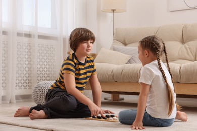 Photo of Cute boy playing checkers with little girl on floor in room