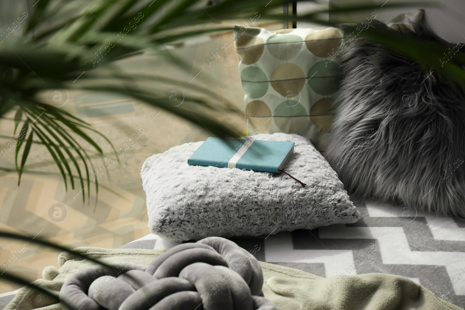 Photo of Notebook, soft pillows and plaids on window sill in room. Cozy place to relax