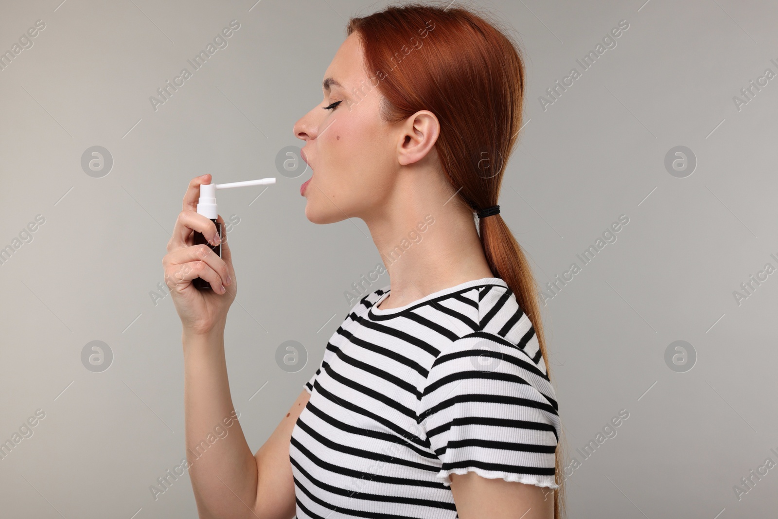 Photo of Young woman using throat spray on grey background