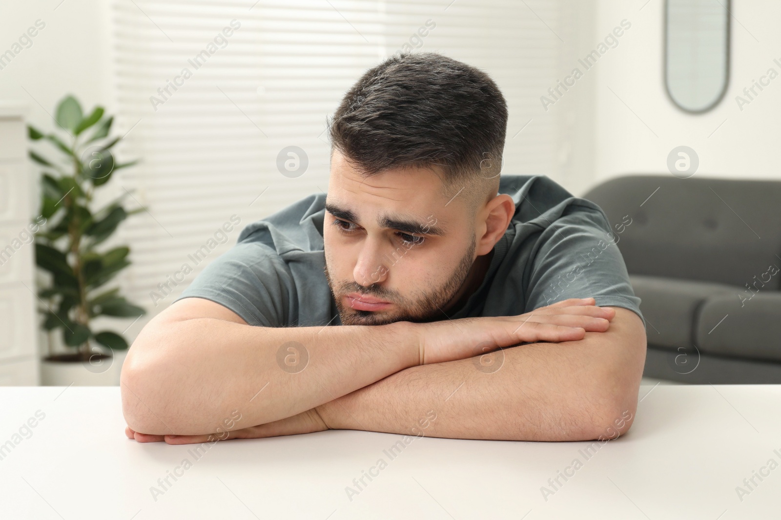 Photo of Sad man sitting at white table indoors