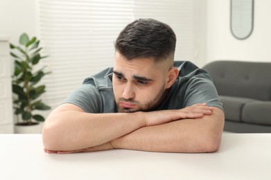 Sad man sitting at white table indoors