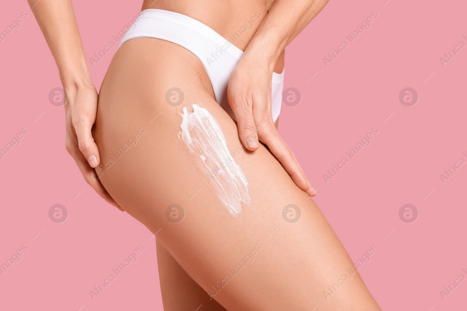 Photo of Woman applying body cream onto her leg against pink background, closeup. Space for text