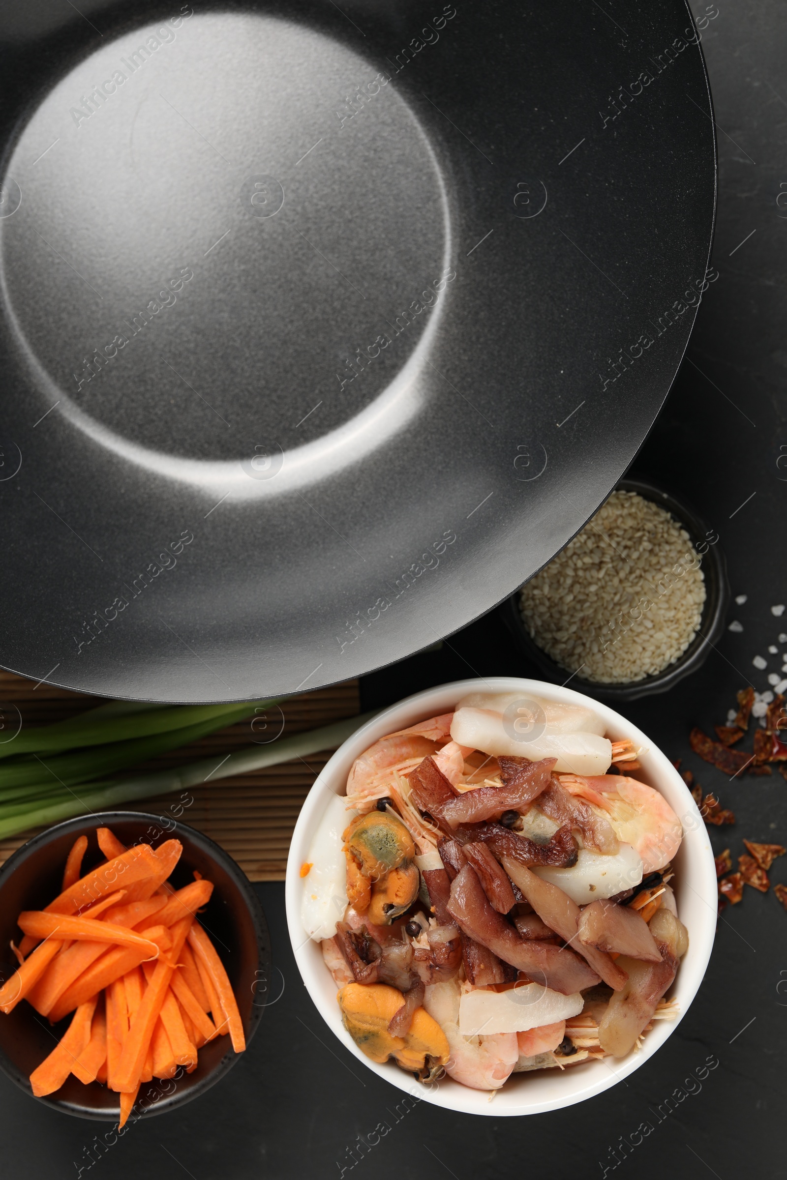 Photo of Black wok, spices and products on dark table, flat lay