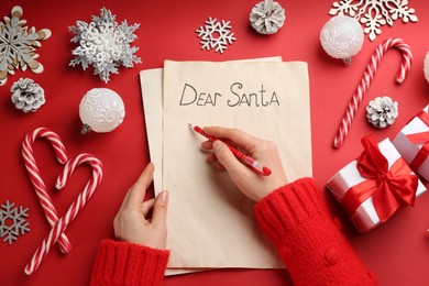 Photo of Top view of woman writing letter to Santa at red table, closeup