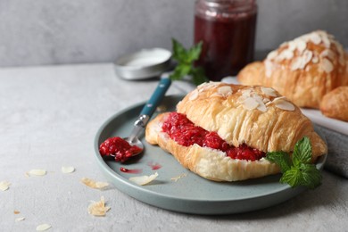 Delicious croissant with berry jam, almond flakes and spoon on grey table, space for text