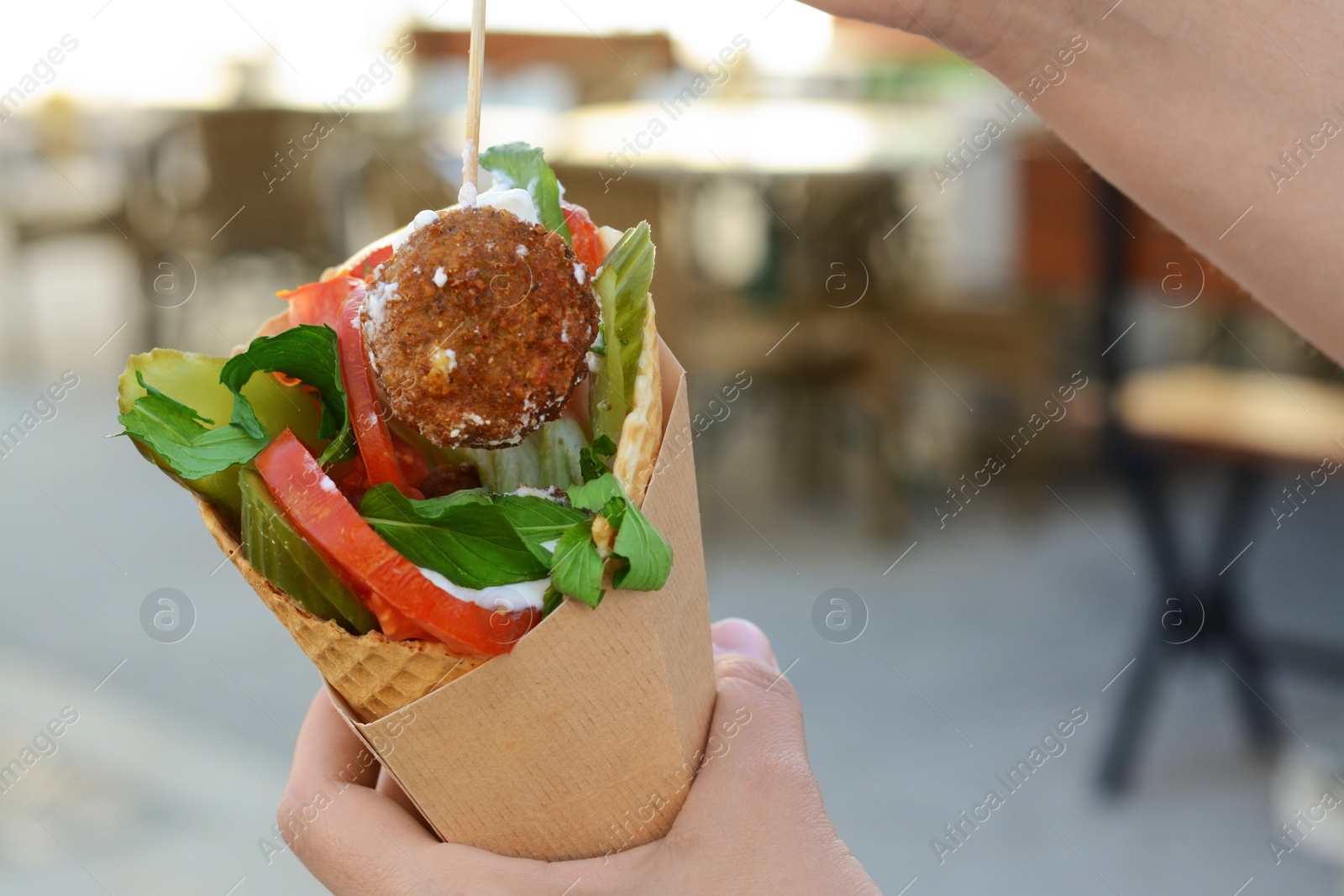 Photo of Woman eating wafer with falafel and vegetables outdoors, closeup. Street food