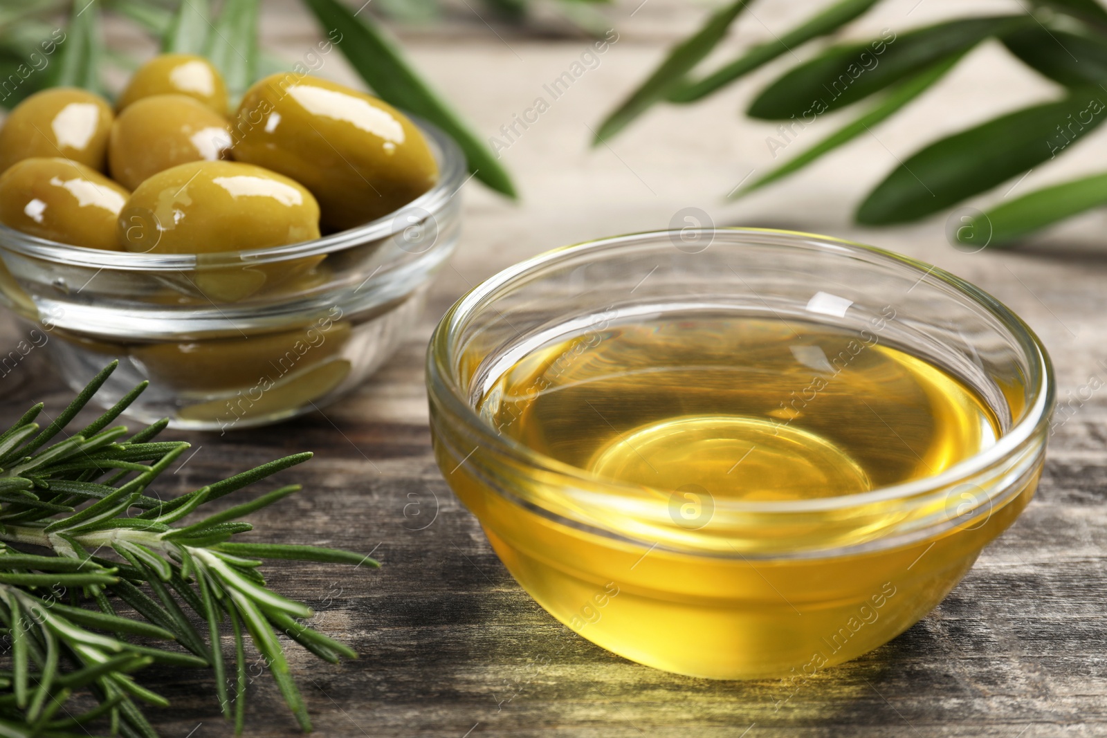 Photo of Cooking oil, olives and rosemary on wooden table, closeup