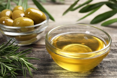 Photo of Cooking oil, olives and rosemary on wooden table, closeup