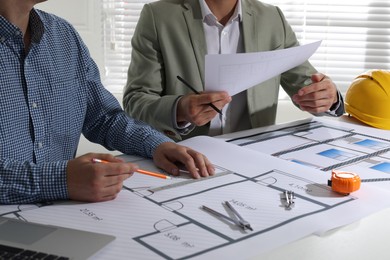 Photo of Architects working with construction drawings at table in office, closeup