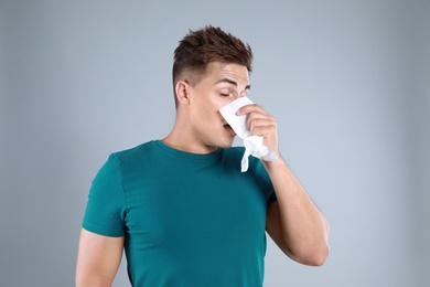 Photo of Young man suffering from allergy on grey background