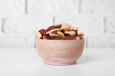 Photo of Bowl with tasty Brazil nuts on white table against brick wall