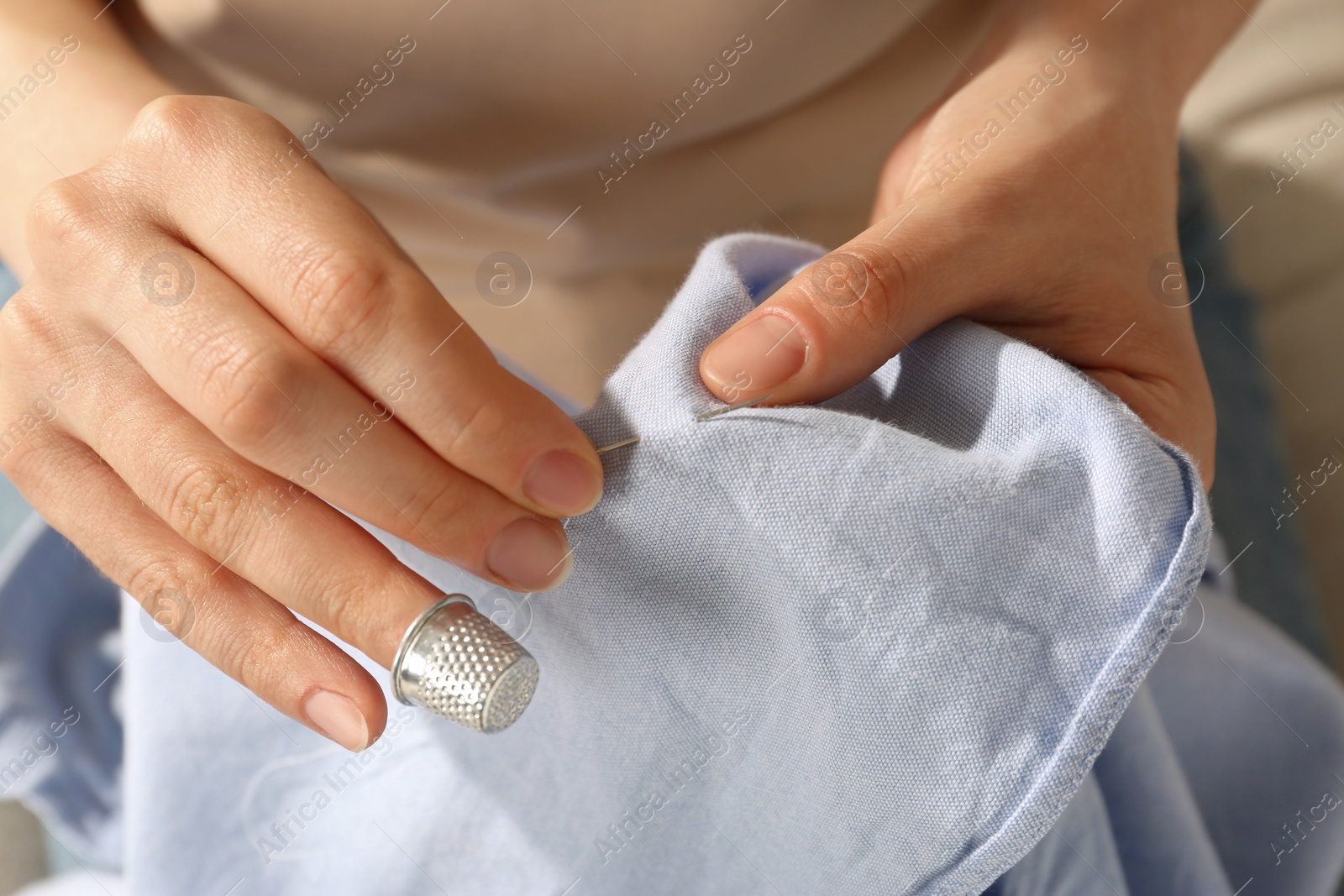 Photo of Woman sewing on light blue fabric with thimble and needle, closeup