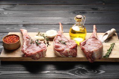 Photo of Fresh tomahawk beef cuts, spices and oil on black wooden table