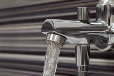 Photo of Water flowing from bath tap on blurred background, closeup