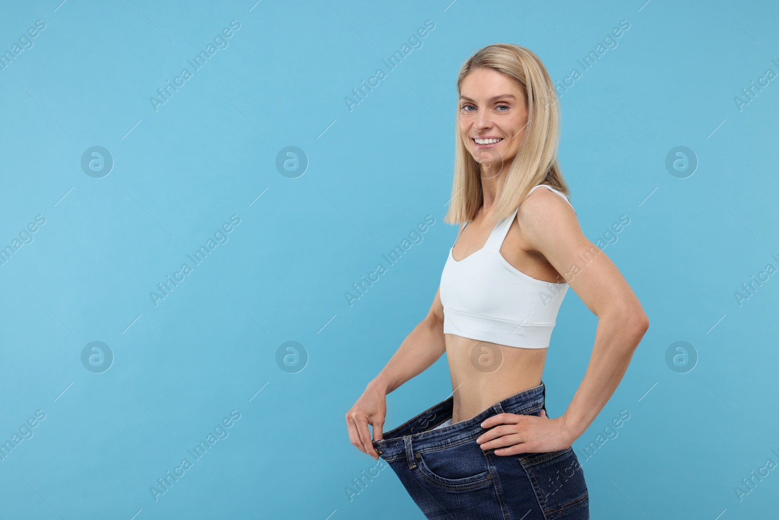 Photo of Slim woman wearing big jeans on light blue background, space for text. Weight loss