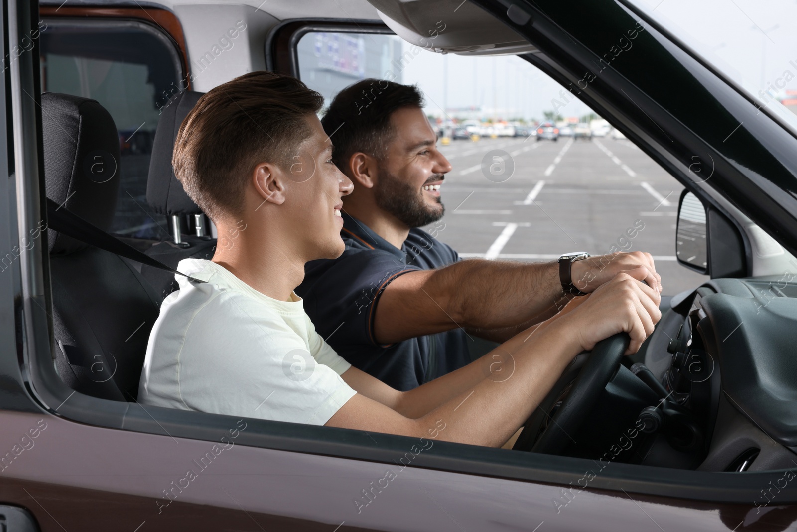 Photo of Driving school. Student during lesson with driving instructor in car at parking lot