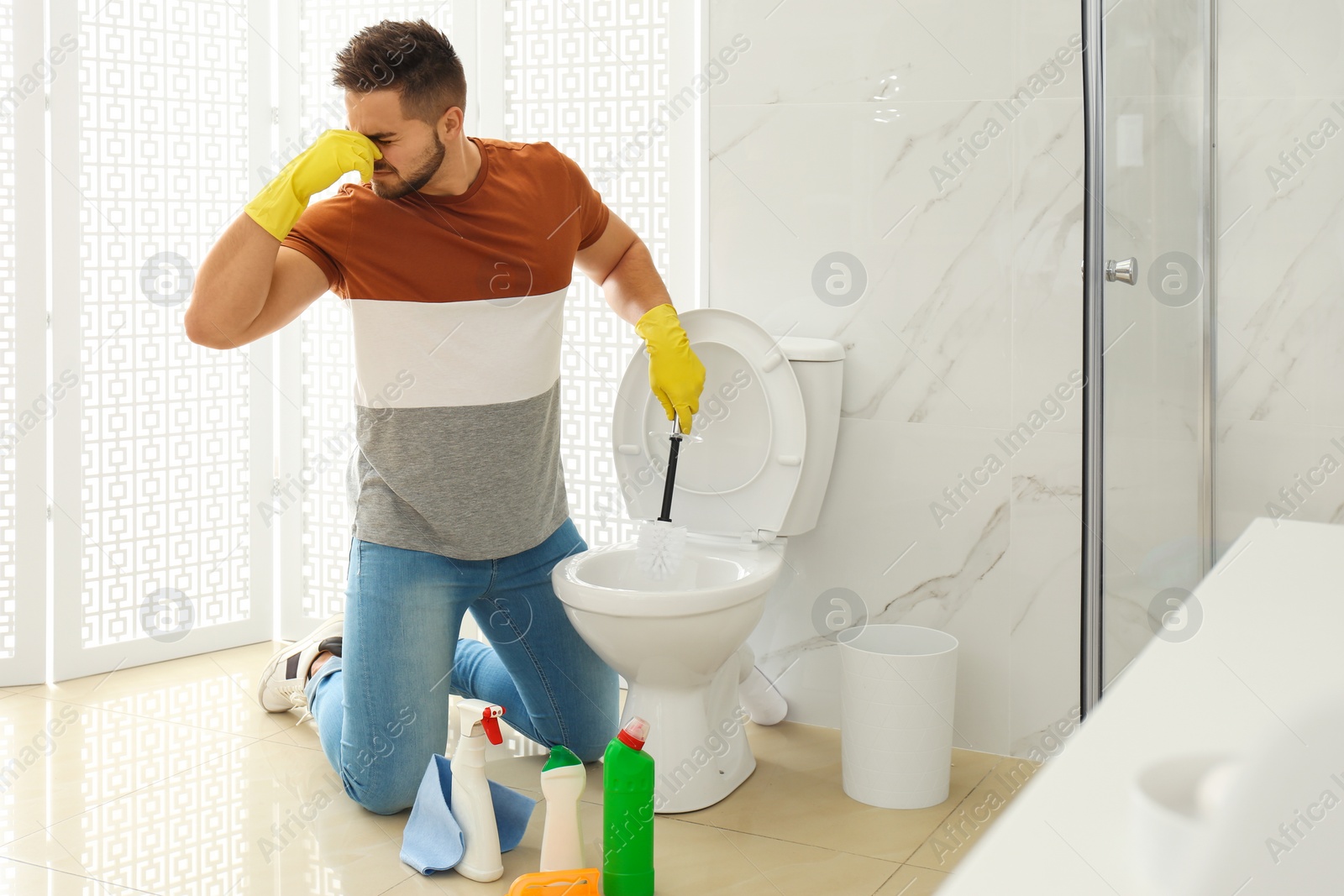 Photo of Young man feeling disgust while cleaning toilet bowl in bathroom