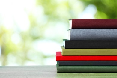 Image of Many stacked hardcover books on wooden table against blurred background, space for text