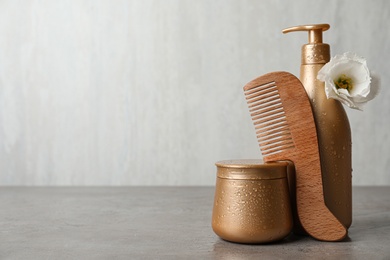 Different hair products, flower and wooden comb on grey table. Space for text