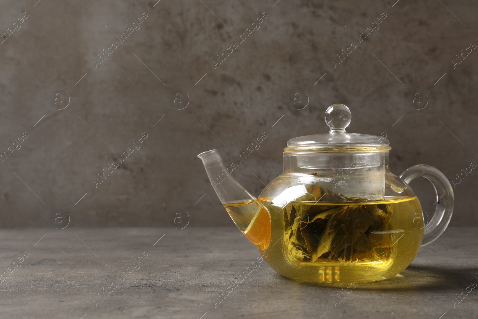 Photo of Glass teapot with oolong on table against grey background. Space for text