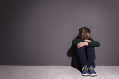 Photo of Depressed little boy sitting on floor indoors. Time to visit child psychologist