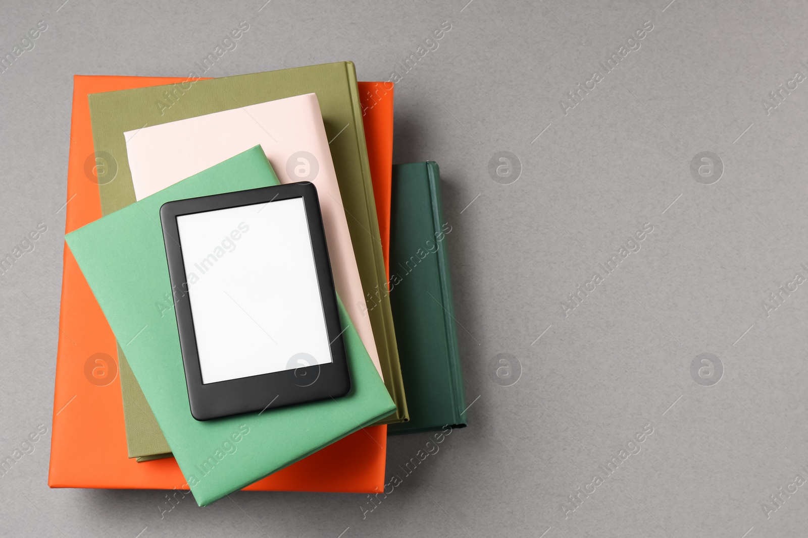 Photo of Modern e-book reader and stack of hard cover books on light grey table, top view. Space for text