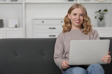 Beautiful woman with blonde hair using laptop on sofa indoors. Space for text