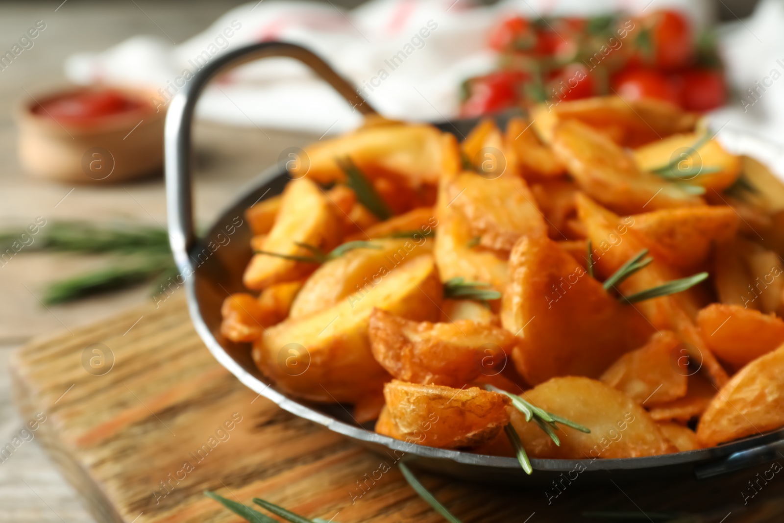 Photo of Metal dish with baked potatoes and rosemary on wooden board, closeup