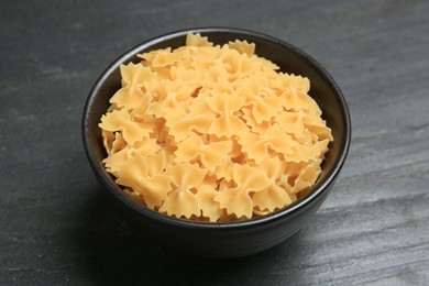 Photo of Raw farfalle pasta in bowl on grey table, closeup