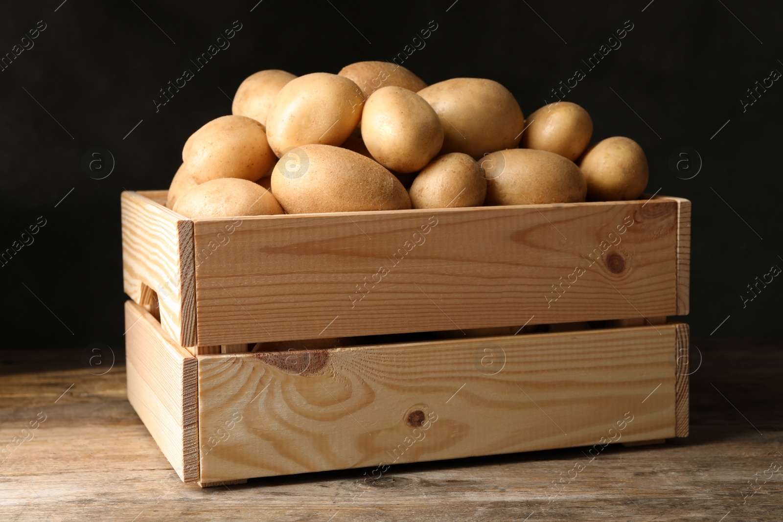 Photo of Raw fresh organic potatoes on wooden table against dark background