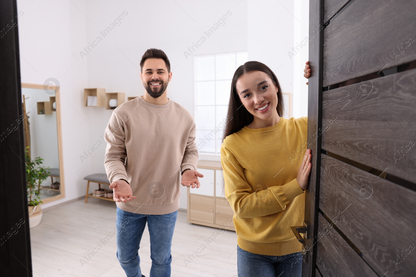 Photo of Happy couple welcoming at home. Invitation to come indoors