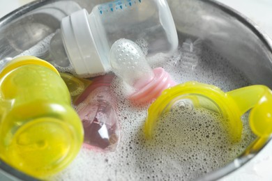 Photo of Metal bowl with baby bottles on white table, closeup