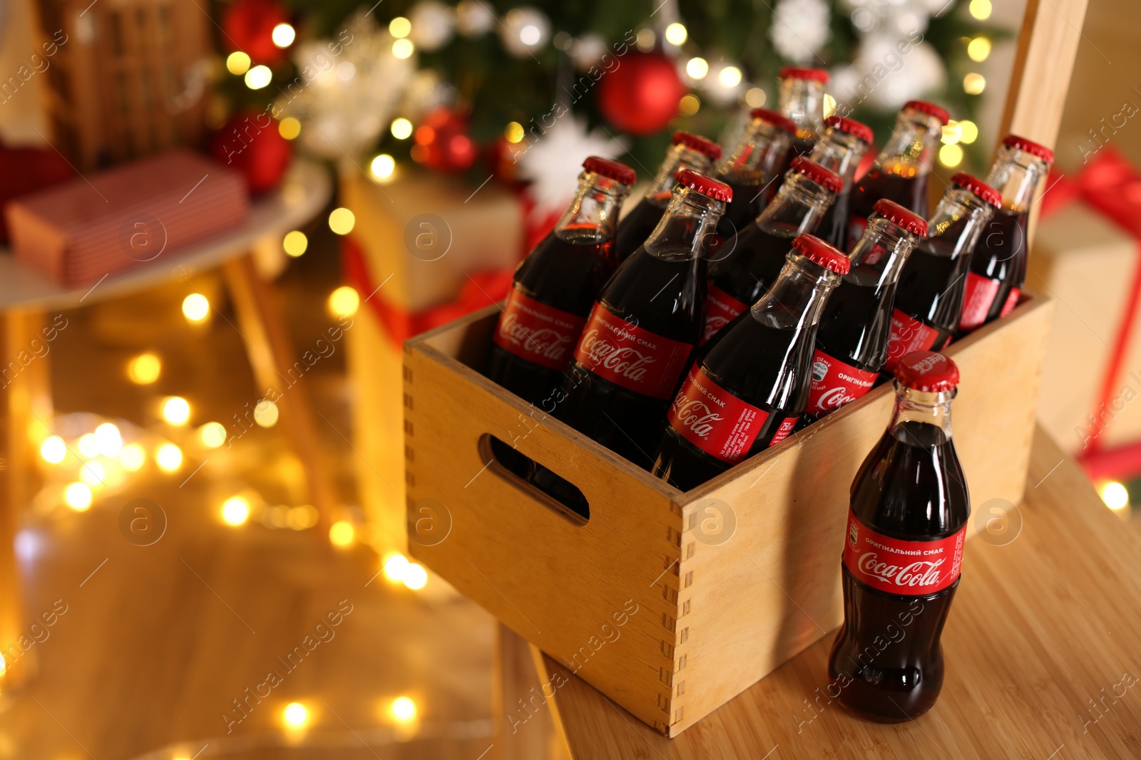 Photo of MYKOLAIV, UKRAINE - JANUARY 18, 2021: Wooden crate with Coca-Cola bottles on chair in room