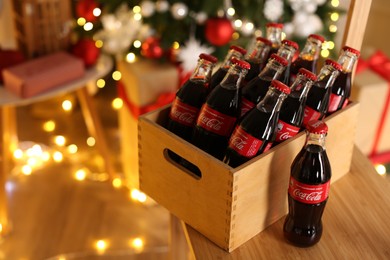 Photo of MYKOLAIV, UKRAINE - JANUARY 18, 2021: Wooden crate with Coca-Cola bottles on chair in room