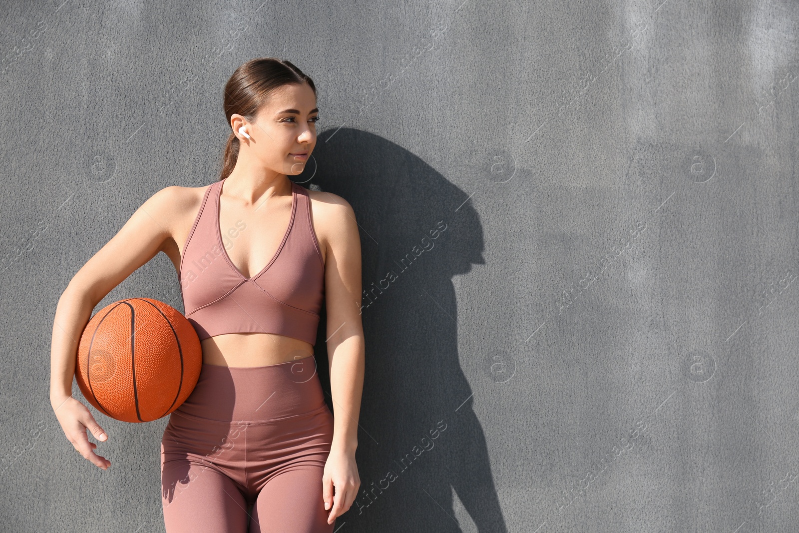 Photo of Young woman in stylish sports wear holding ball on grey background. Space for text