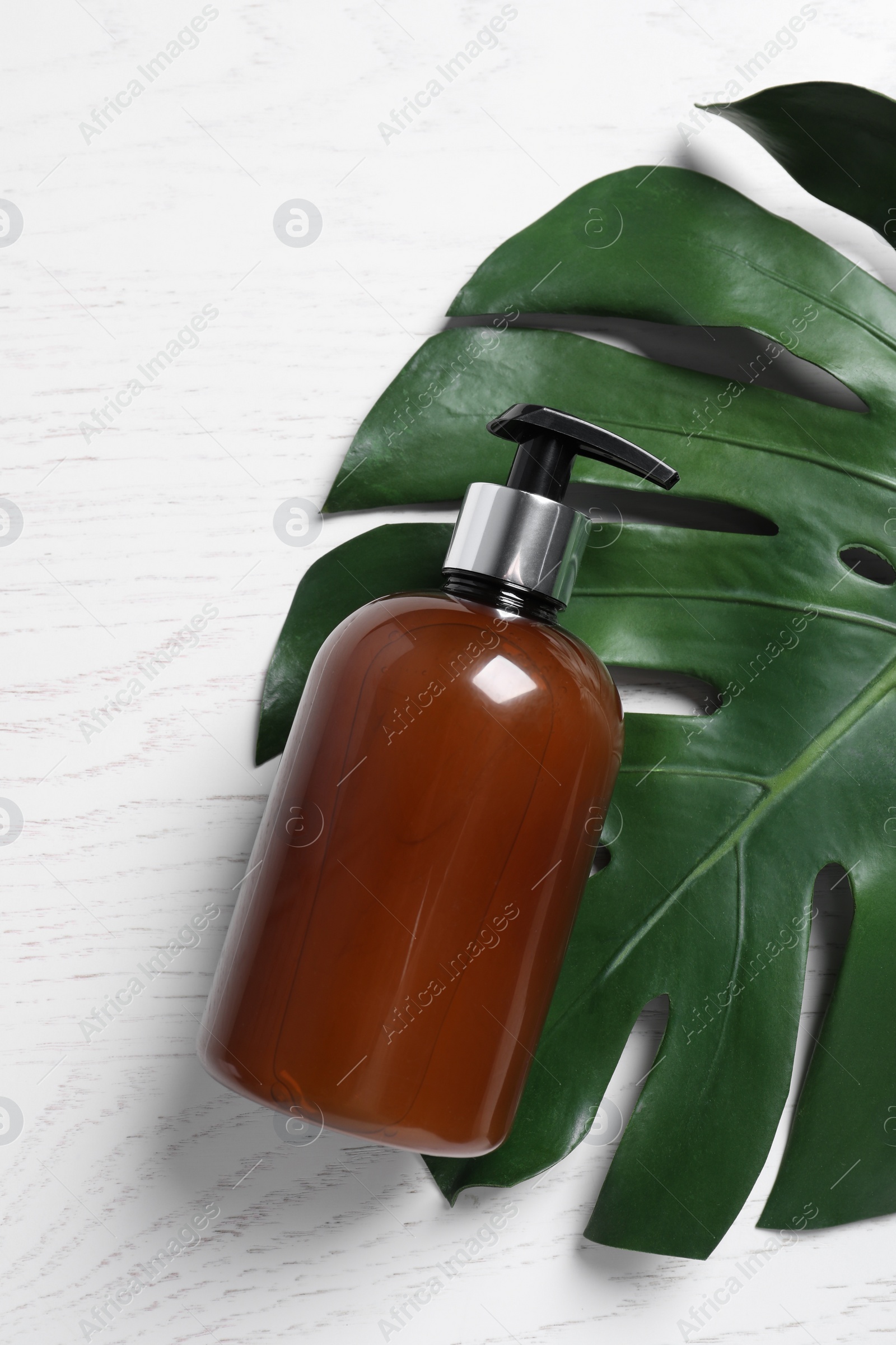 Photo of Bottle of cosmetic product and leaf on white wooden table, flat lay