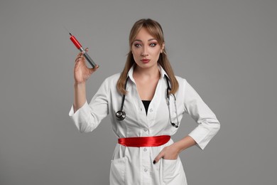 Photo of Woman in scary nurse costume with syringe on light grey background. Halloween celebration