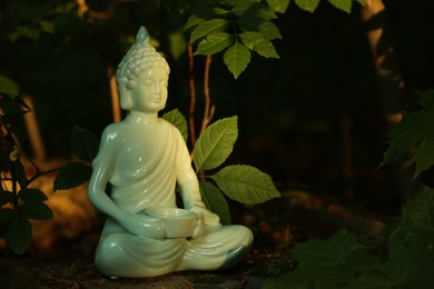 Decorative Buddha statue on stone under tree, space for text